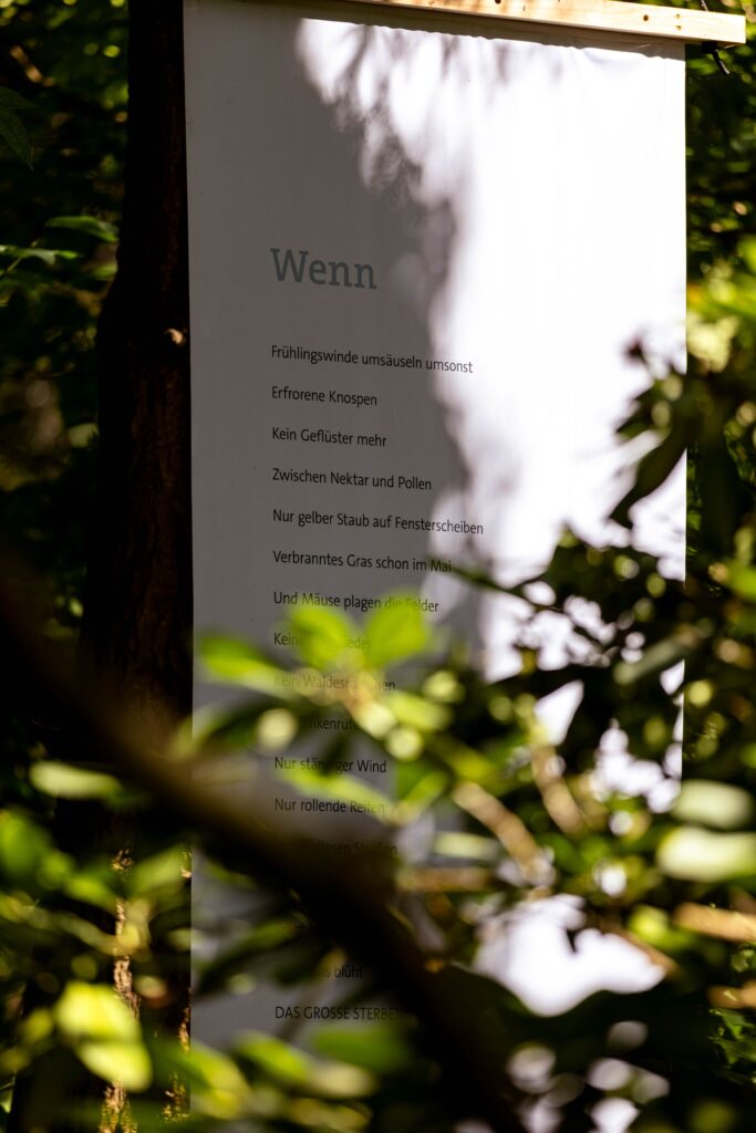 Ein großer Banner mit dem Gedicht "Wenn" hängt zwischen grünen Zweigen. © Max Winkler